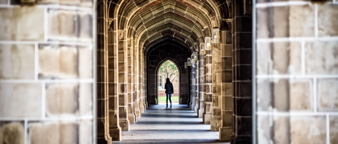 A stone arch hallway at a university with unidentified female in the distance